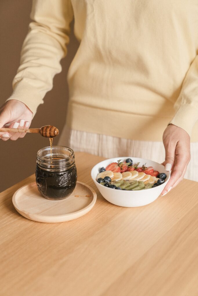 Woman pouring honey on fruit bowl to show that all foods fit