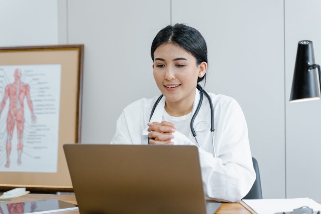 A doctor in a white coat looking at a computer, administering a telehealth visit with a patient
