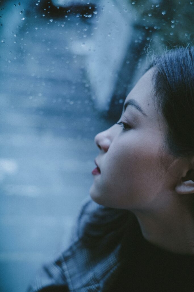 Pensive older child looking out a window with rain specks